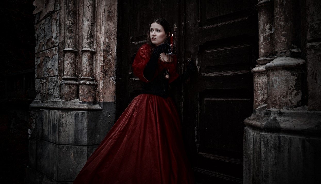 Mysterious woman in red Victorian dress with a candle